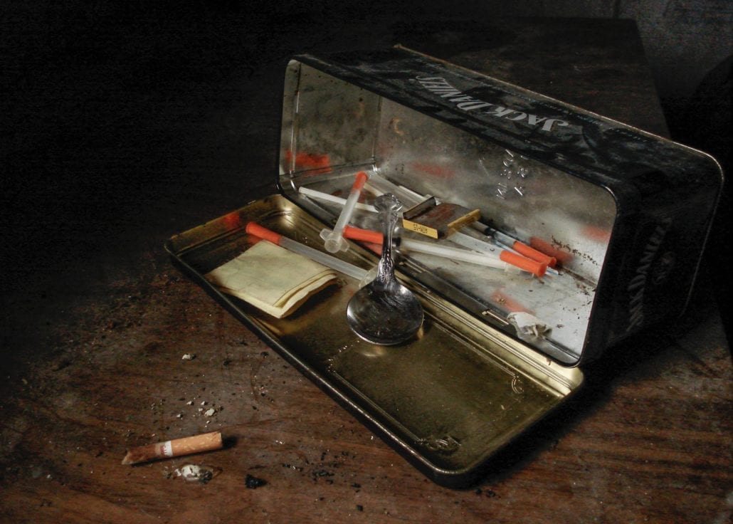clear and red syringes inside open tin can near cigarette butt